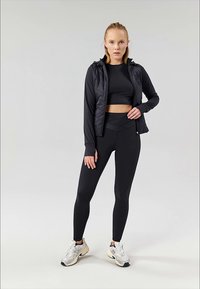 Svartidrettsantrekk bestående av en tettsittende crop top, slanke leggings og en zip-up hettegenser med quiltet mønster. Teksturert joggebukse og joggesko.