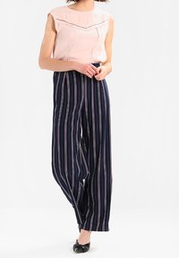 Light pink sleeveless top with ruffled edges paired with navy and pink striped wide-leg pants. Black flats complete the outfit.