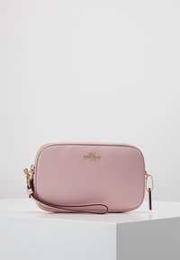 Vaaleanpunainen nahkainen olkalaukku, jossa on kivipinta, kultaiset yksityiskohdat, vetoketjukiinnitys ja irrotettava rannetuki. Coach-logo etupuolella.