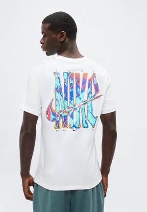 Jonge man die zijwaarts kijkt, draagt een wit T-shirt met een kleurrijke, abstracte "JUST DO IT" en Nike swoosh afbeelding op de rug.