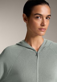 Svijetlozelena rebrasta dukserica s patentnim zatvaračem koja ima kapuljaču, teksturiranu tkaninu i središnji patentni zatvarač. Dizajn ima raglan rukave za udobnost.