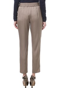 Osoba w taupe'owych prostych spodniach z elastycznym pasem i ciemnych, wysokich butach na obcasie, pokazana od tyłu.