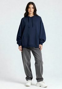 Felpa con cappuccio blu navy con tasca a marsupio, vestibilità oversize, polsini a coste, indossata con jeans grigi e sneakers bianche, texture liscia.