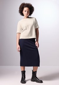 Licht beige top met korte mouwen gecombineerd met een donkerblauwe geribbelde midi-rok. Het model draagt zwart enkellaarsjes met stevige zolen.