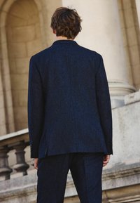 Marineblauer Tweed-Anzug mit strukturiertem Design. Verfügt über einen Reverskragen und geknöpfte Manschetten. Der Stoff hat eine strukturierte Oberfläche und eine taillierte Passform.