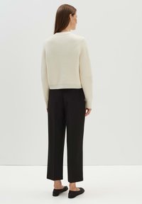 Cremfarbener Pullover mit lockerer Passform und geripptem Saum, kombiniert mit schwarzen weitgeschnittenen Hosen und schwarzen flachen Schuhen. Minimalistisches Design.