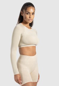 Top court à manches longues beige et shorts taille haute en tissu extensible. Texture lisse avec des accents côtelés subtils sur l'ourlet et la ceinture.