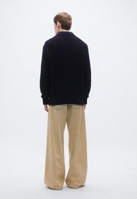 Tengerészkék kötött kardigán texturált mintával, bézs színű, bő szárú nadrággal, hátul zsebekkel. Egyszerű, laza szabás.