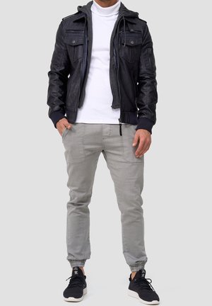 Black leather bomber jacket with hoodie, zippered pockets, gray tapered pants, and black sneakers with white accents.