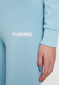 Ljusblå sportkläder med ribbad mudd och Hummel-logotyp i vitt. Slät textur, åtsittande design som betonar komfort och funktionalitet.