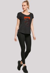 Black short-sleeve t-shirt with a graphic design featuring the word "PANTERA" and a snake. Paired with black leggings and sneakers.