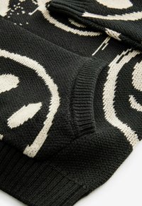 Czarny sweter z dzianiny z białymi okrągłymi wzorami, z żeberkowymi mankietami i dołem, o teksturowanym wykończeniu oraz kontrastujących kolorach.