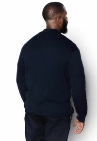 Námornícky modrý pulóver s dlhým rukávom v klasickom strihu, s rebrovanými manžetami a rovnou golierom. Mäkká štruktúrovaná tkanina, minimálne dizajnové akcenty.