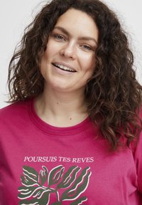 Fuchsiové tričko s krátkými rukávy, kulatým výstřihem, s bílým grafickým motivem listů a textem "POURSUIS TES REVES" nahoře.