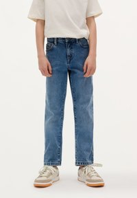 Lysblå denimjeans med lige snit, fem-lommer design og subtile stikninger, parret med beige og hvide sneakers.