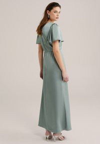 Long, soft, mint green satin dress with short flutter sleeves, a fitted waist, and a flowy skirt, paired with metallic heeled sandals.