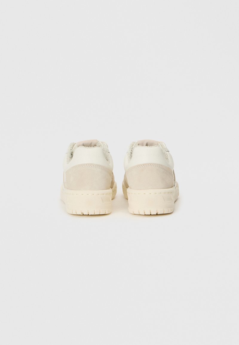 Zapatillas blancas y beige con acentos de ante, punta redonda, suela de goma texturizada, y cuello y lengüeta acolchados parcialmente visibles.