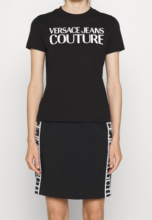 Zwarte top met korte mouwen met de tekst "Versace Jeans Couture", gecombineerd met een bijpassende zwarte rok met witte logostrepen aan de zijkanten.