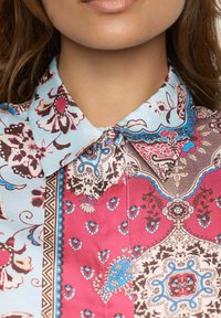 Multikleurige blouse met een bloemenprint in tinten van roze, blauw en bruin. Gekraagde ontwerp met knopen en ingewikkelde patronen.