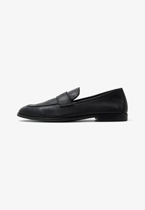 Black leather loafers with a rounded toe, detailed stitching, and a flat sole. The design features a subtle raised strap across the vamp.