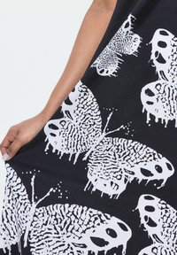 Schwarzer Stoff mit großen weißen Schmetterlingsdrucken, die intricate Details und Tropfmuster aufweisen. Die Textur wirkt glatt und betont den Kontrast.