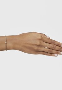 Bracciale d'argento delicato con piccole perline distribuite uniformemente e una perla centrale più grande, esposto su una mano su uno sfondo neutro.