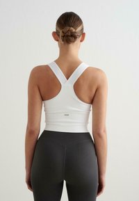 Valkoinen urheilullinen crop-top, jossa on paksut olkaimet. Ribattua tekstuuria ja istuva muotoilu. Yhdistetty korkeavyötäröisiin harmaisiin ribattuihin legginsseihin.