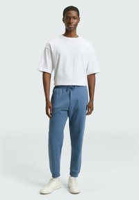 Biała koszulka z krótkim rękawem, jasnoniebieskie spodnie dresowe z elastycznymi mankietami, ściągaczem w pasie i subtelnym logo. Całość dopełniają białe trampki.