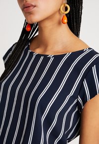 Top blu navy con strisce verticali bianche, dotato di scollatura rotonda e maniche corte. Tessuto testurizzato con una finitura liscia.
