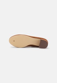 Scarpa in suede marrone con punta tonda e tacco basso a blocco. La suola è in gomma beige liscia, con un leggero motivo di aderenza.