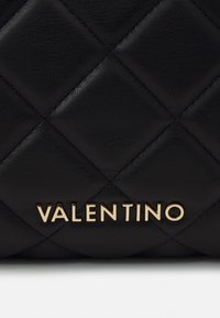 Black leather handbag with a quilted pattern, featuring a prominent gold "VALENTINO" logo. Textured surface with diagonal stitching accents.