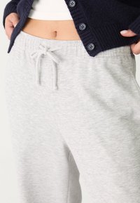 Lichtgrijze joggingbroek met een trekkoord in de taille en een soepele textuur, gecombineerd met een donkerblauwe gebreide cardigan met grote knopen.