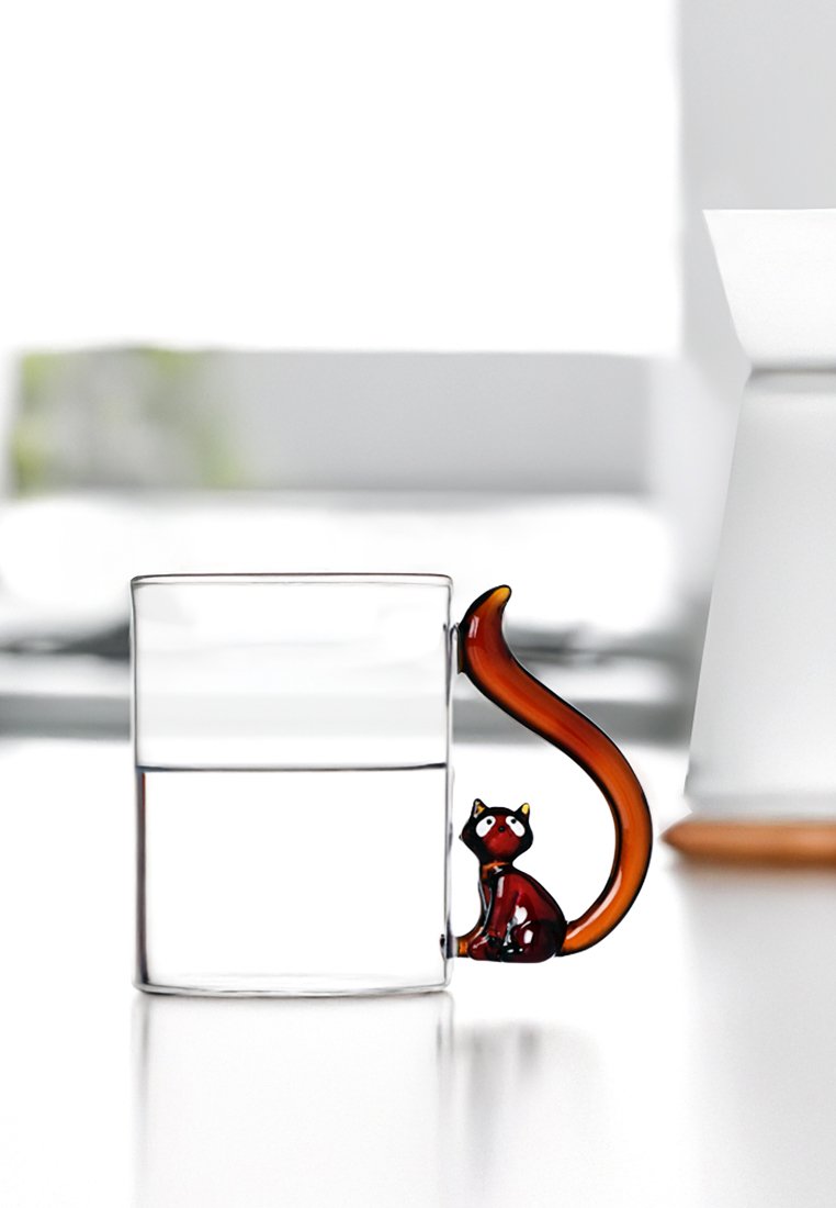 Klares Glasbecher mit einem katzenförmigen, braunen Griff und einem kleinen, sitzenden Katzenmuster. Enthält Wasser; einfacher, moderner Stil.