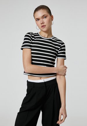 Musta-valkoiraaita lyhythihainen cropped t-paita, jossa on ribbattu pinta ja kontrastivärinen pääntie, yhdistettynä korkeavyötäröisiin mustiin housuihin.