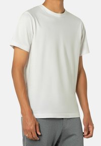 Weißes Baumwoll-T-Shirt mit Rundhalsausschnitt, kurzen Ärmeln und lockerer Passform, kombiniert mit grauen strukturierten Hosen.