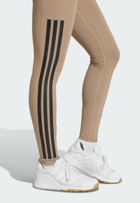 Tan leggings with three vertical black stripes on the sides, paired with white athletic shoes featuring a textured design and rubber sole.