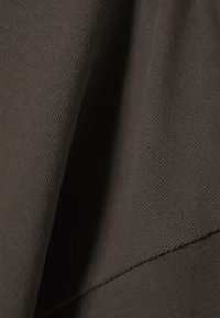 Bruine katoen stof met een zachte, textuurrijke oppervlakte en zichtbaar breipatroon; heeft een gevouwen, gelaagd ontwerp.