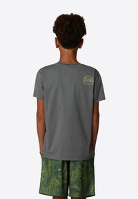 Camiseta gris de manga corta hecha de algodón con cuello redondo, que presenta un diseño de logo verde en la parte superior de la espalda. Combinada con pantalones cortos verdes con patrón.