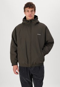 Veste zippée vert olive avec capuche, poignets élastiques et ourlet, arborant un logo sur la poitrine, conçue pour une coupe décontractée.