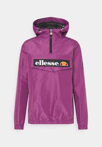 Fioletowa kurtka przeciwwiatrowa z kołnierzem na półzamek, elastycznymi mankietami, przednią kieszenią oraz czarną naszywką z logo.