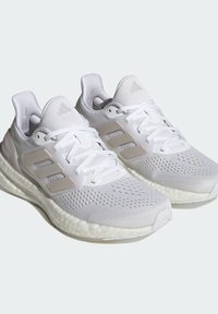 Witte sportschoenen met een ademend bovenwerk van mesh, textuurpatronen en een gevoerde zool. Kenmerkende drie strepen als een subtiele accent.