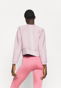 Sweat-shirt rose clair texturé avec manches raglan et ourlet côtelé, associé à des leggings roses ajustés ornés d'un logo blanc sur le côté.