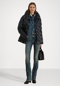 Black quilted puffer jacket with a high collar, layered over a denim jacket and fitted denim jeans. Black handbag and ankle boots complete the look.