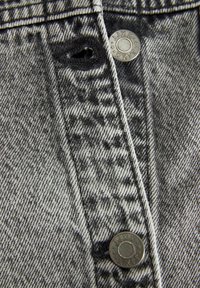 Denim en blanco y negro con una superficie texturizada. Presenta un botón plateado con marcas y un pequeño agujero cerca del botón.