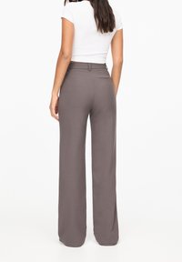 Pantalons gris à jambes larges avec une texture lisse, dotés d'une taille haute et de poches arrière ; associés à un haut blanc ajusté.