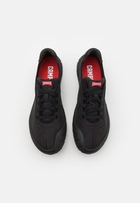 Black athletic shoes made of fabric, featuring a textured surface, lace-up design, rubber sole, and red "CAMPPER" logo on the insole.