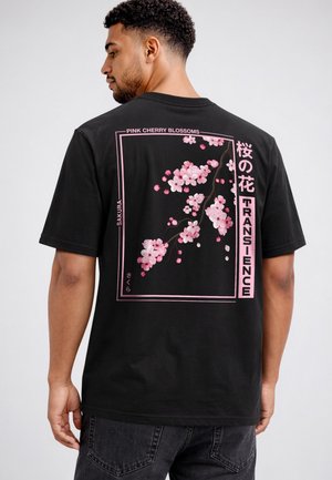 Man wearing black t-shirt with pink cherry blossom branch and text "PINK CHERRY BLOSSOMS," "SAKURA," and Japanese characters on back.