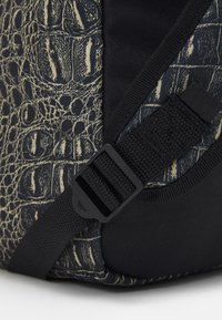 Svart och mönstrad väska med hörn som har ett texturerat krokodil-liknande mönster och ett hållbart rem med plastspänne och textilaccenter.