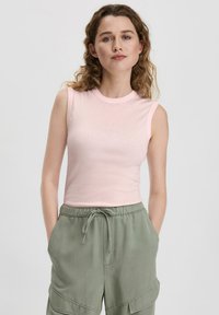 Lichtroze mouwloze top met een ronde hals, gemaakt van zachte stof, gecombineerd met losse groene cargobroeken met zakken.