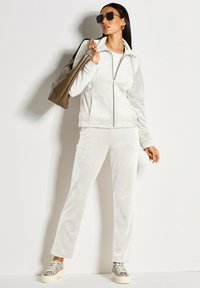 Lichtgrijs velours trainingspak met een jas met ritssluiting en een subtiel luipaardpatroon, gecombineerd met bijpassende broek en sneakers met slangenprint.